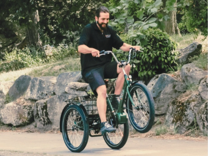 Green e-trike with two back wheels doing a wheelie on a countryside pavement